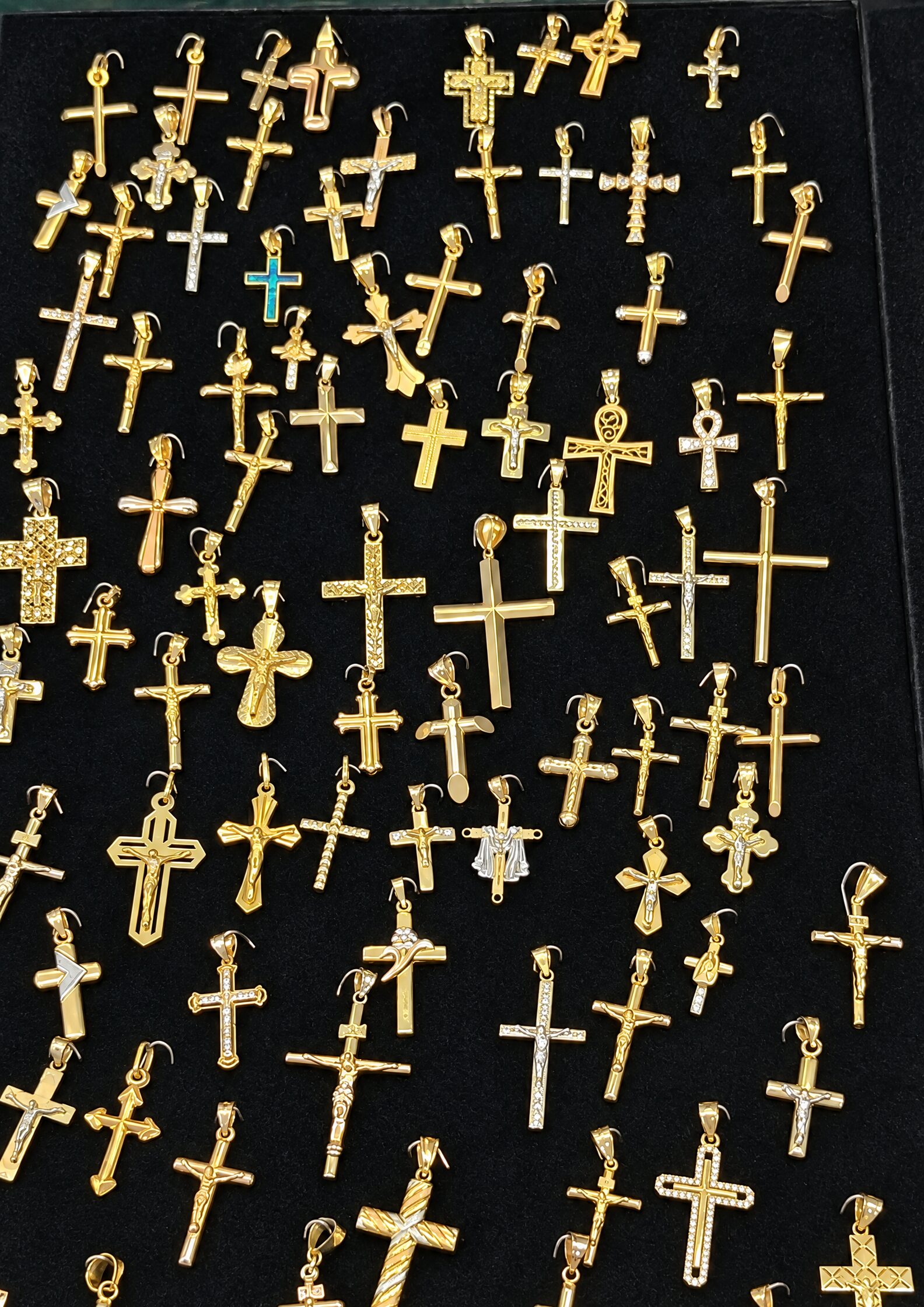 Filas de cruces y crucifijos dorados de muchos tamaños sobre terciopelo negro, algunos con detalles blancos o verdes.