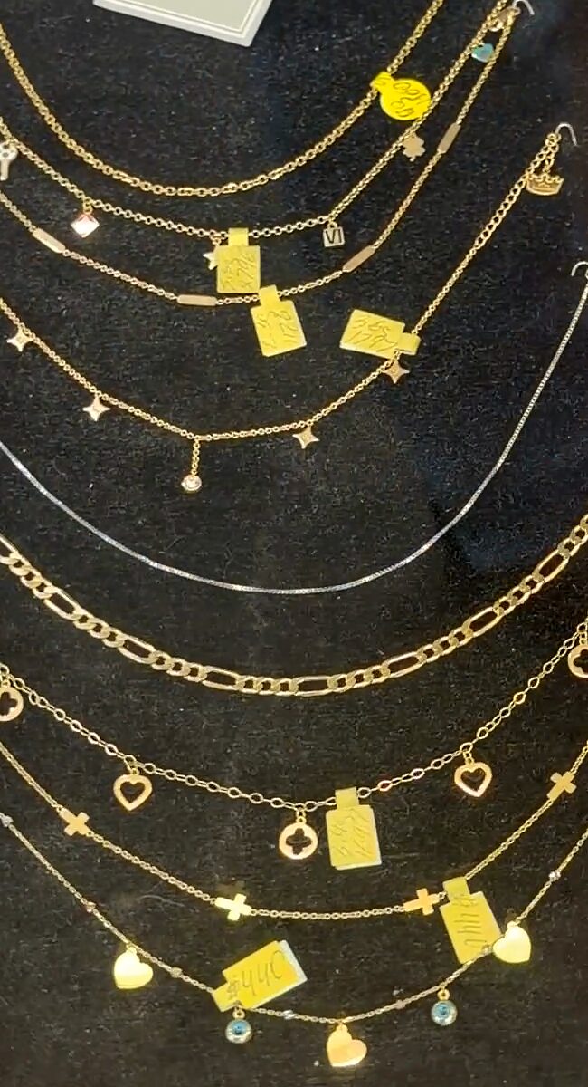 Tobilleras y pulseras doradas finas con dijes pequeños de corazones, estrellas y placas sobre terciopelo negro.