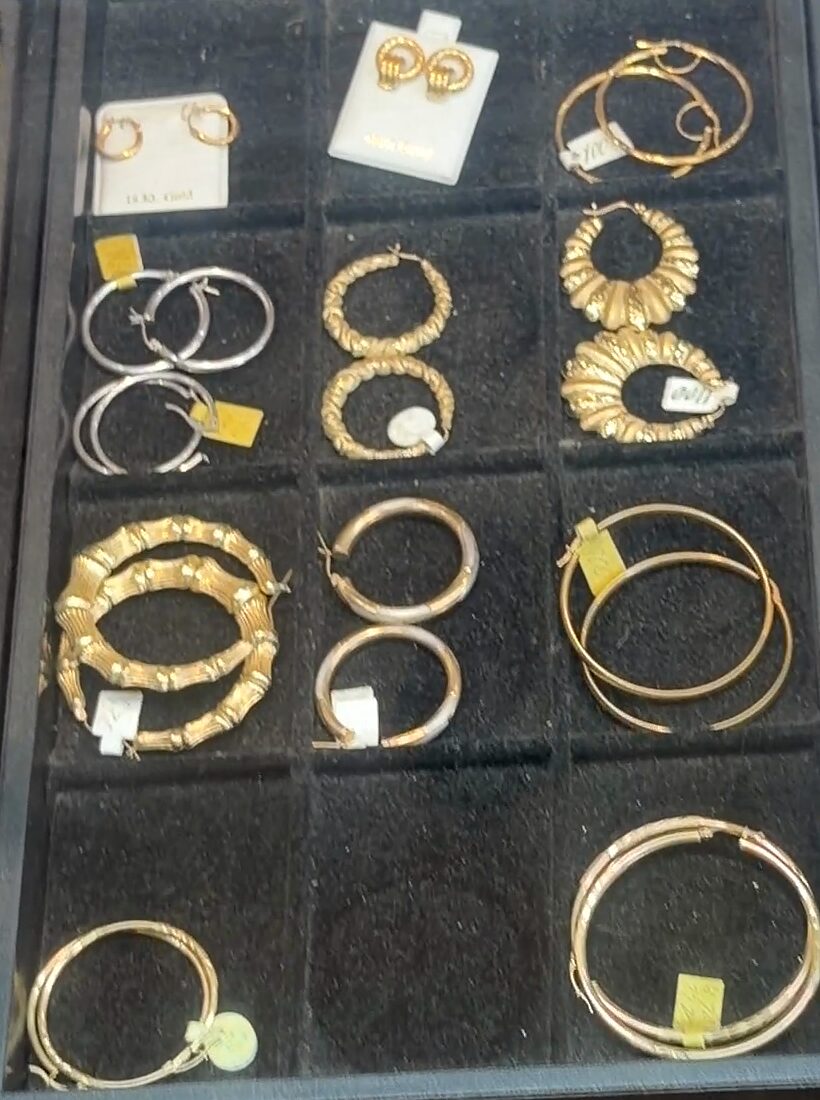 Una bandeja negra de aretes: argollas plateadas y doradas, argollas estilo bambú y aretes pequeños en tarjetas.