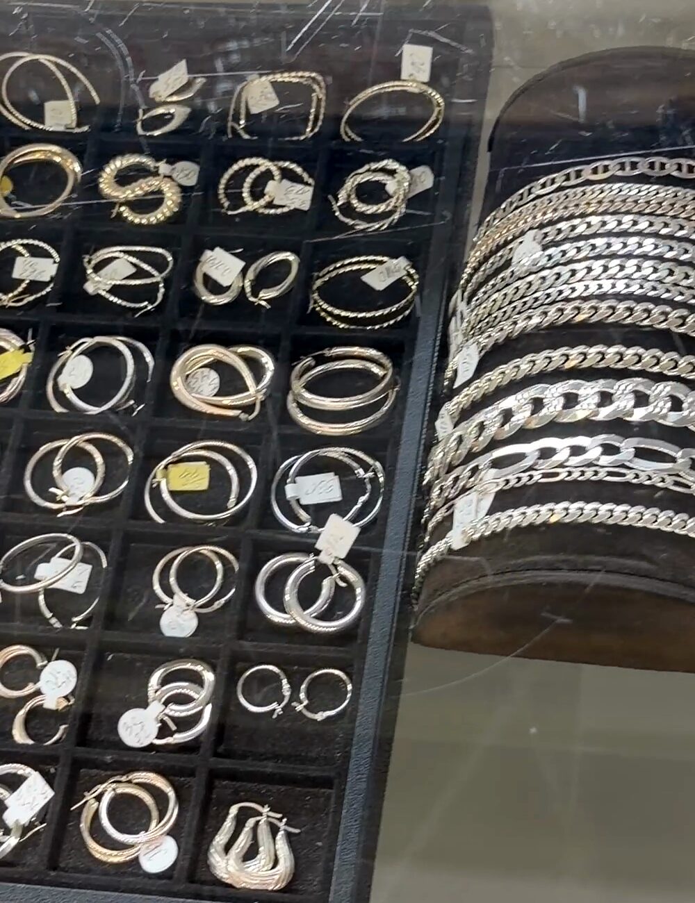 Pulseras plateadas de eslabones apiladas en un rollo oscuro junto a una bandeja de argollas.