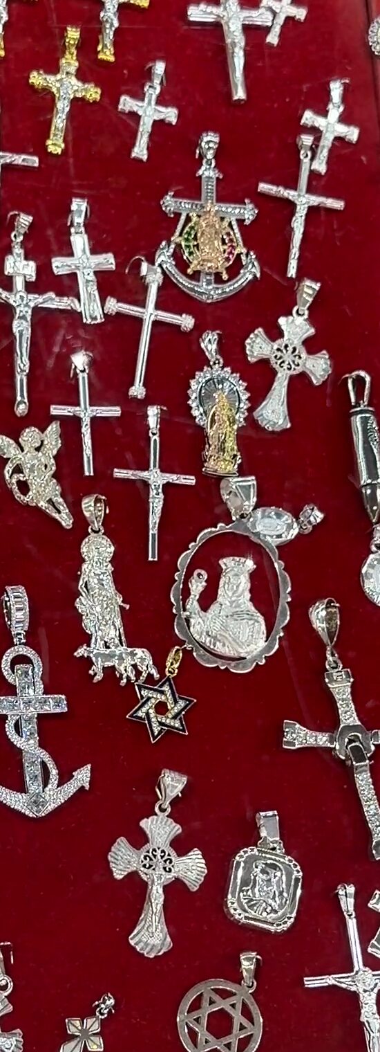 Cruces y crucifijos plateados, un ancla y un dije de la Virgen de Guadalupe sobre terciopelo rojo.