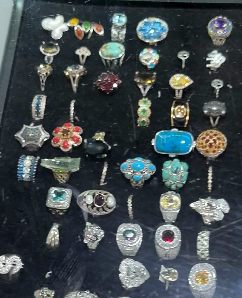 Anillos plateados con piedras turquesa, moradas, rojas, amarillas y verdes sobre terciopelo negro.
