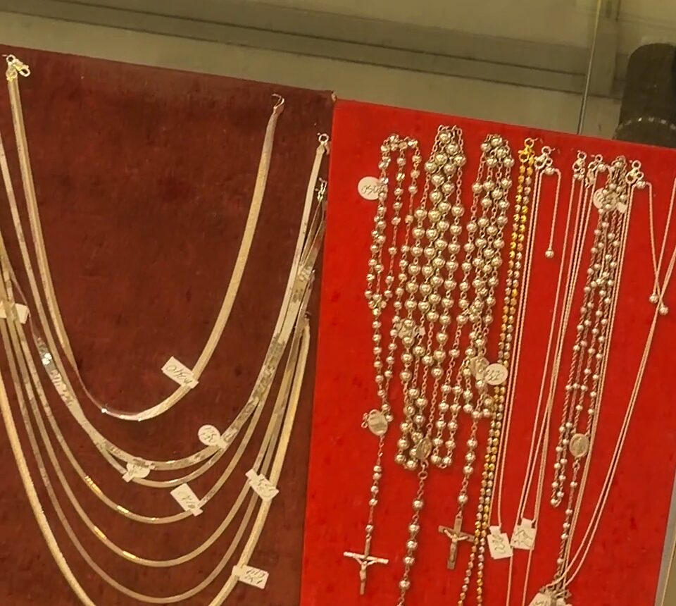 Rosarios plateados con cruces y cadenas finas en tableros de terciopelo rojo dentro de una vitrina.